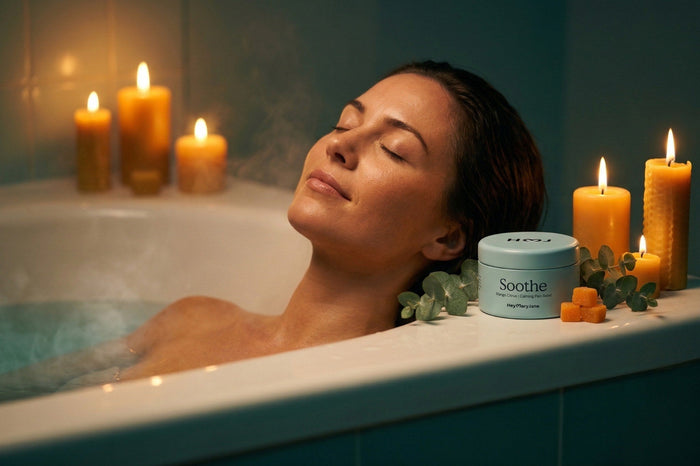 Woman in the bath tub with some candles and a tin of Soothe by HeyMaryJane on the side.