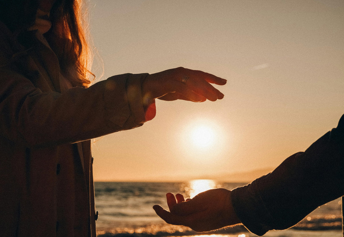 Hands frame the setting sun over the ocean at the beach during golden hour.