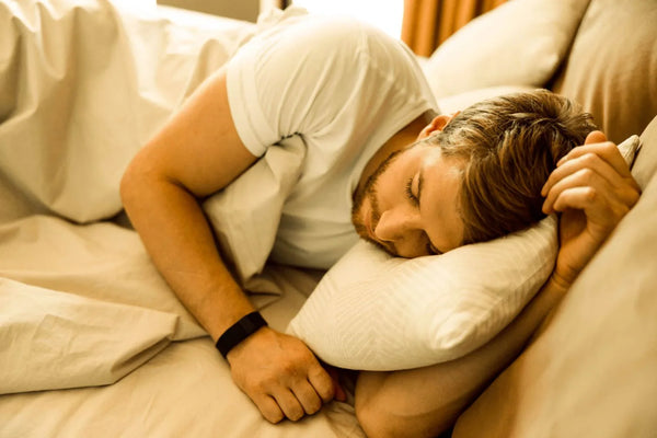 A person sleeps on their side under soft white bedding in warm bedroom light.