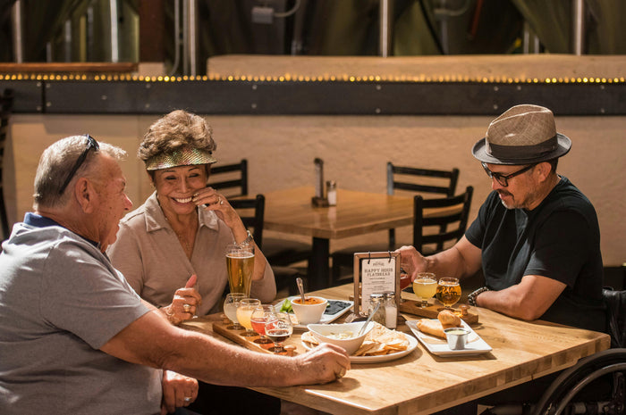 Two adults sit at a warmly lit restaurant table with food, drinks, and cozy evening decor.