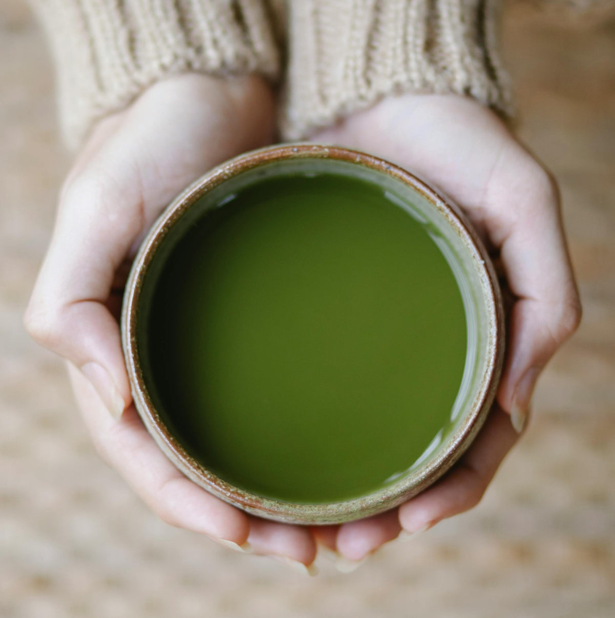 Close-up of hands holding a ceramic cup filled with green tea or matcha.