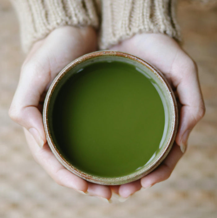 Close-up of hands holding a ceramic cup filled with green tea or matcha.