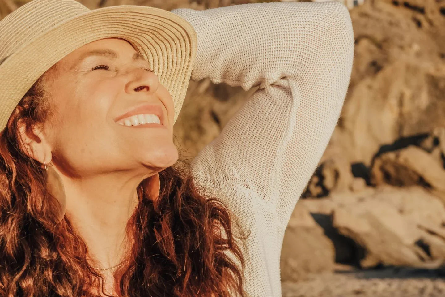 Woman smiling with eyes closed in warm sunlight, enjoying a peaceful moment outdoors with a relaxed, content expression