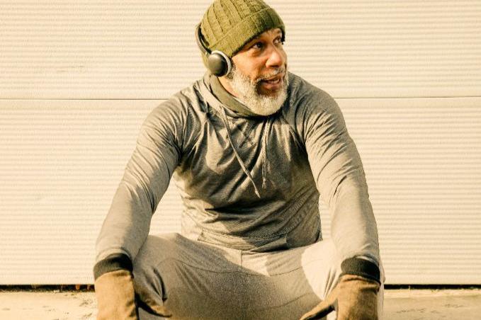 Man in athletic wear sitting outdoors with headphones on, catching his breath after a workout and looking energized, focused, and ready to keep going.